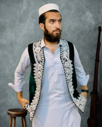 Man wearing a traditional embroidered vest over a white shirt against a gray background