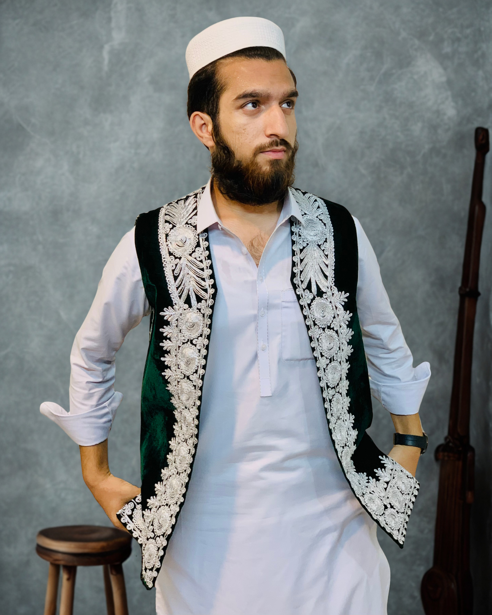 Man wearing a traditional embroidered vest over a white shirt against a gray background