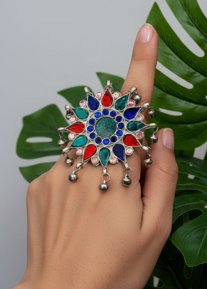 Decorative pendant with colorful stones held in a hand against a yellow background