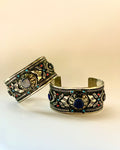 Two ornate bracelets with intricate designs and colorful stones on a beige background