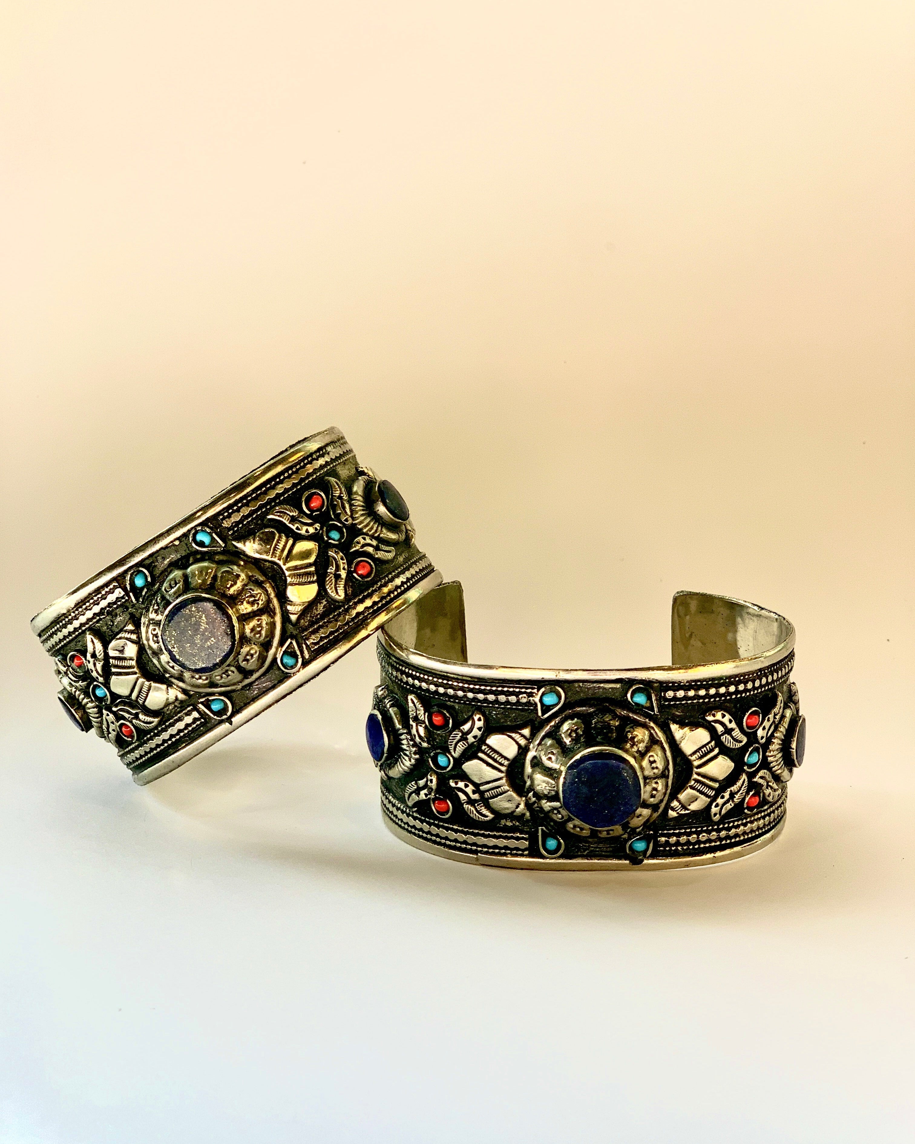 Two ornate bracelets with intricate designs and colorful stones on a beige background