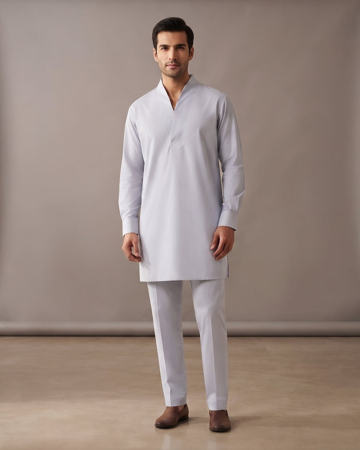 A man modeling a light gray long-sleeve kurta and matching trousers in a studio setting with a beige backdrop.