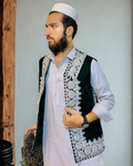 Man wearing a traditional embroidered vest over a light shirt with a plain background